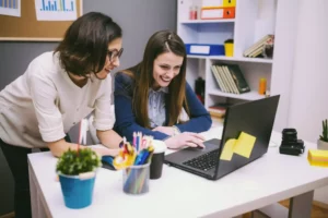 Two women working on a laptop in an office.