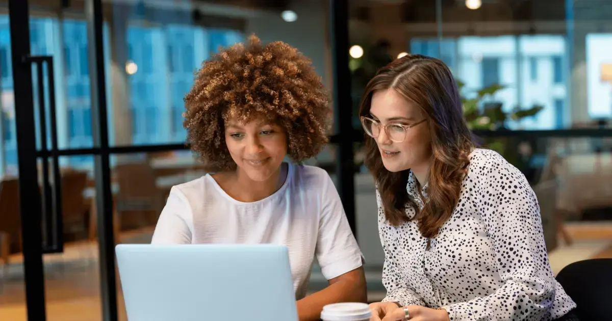 Two women working on a laptop in an office.