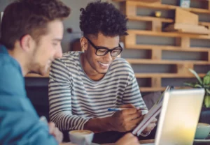 Two young men working on a laptop in a coffee shop.