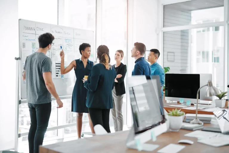 A group of people standing around a whiteboard in an office.