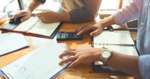 Three people working at a desk with papers and a calculator.