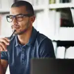 A man in glasses is looking at a computer screen.