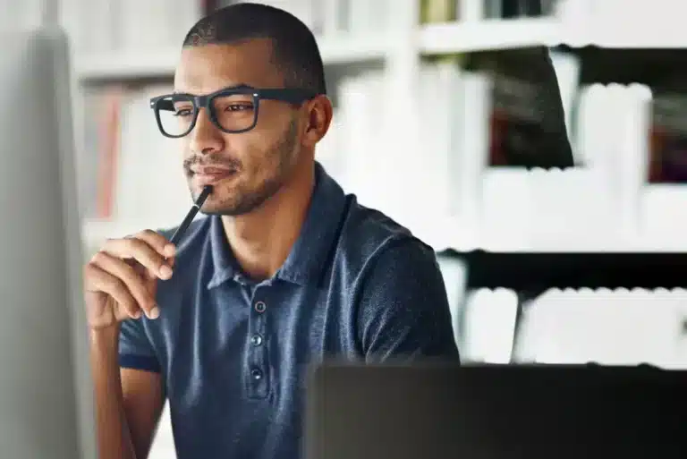 A man in glasses is looking at a computer screen.