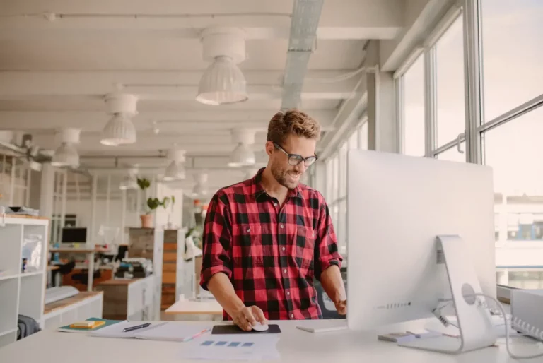 A man in a plaid shirt is working on a computer in an office.