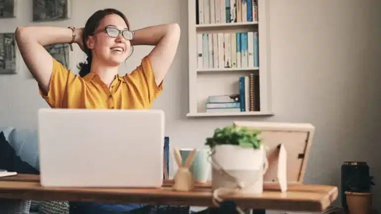 A woman is sitting at a desk with her hands raised in the air.