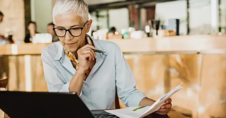 An older woman sitting at a table with a laptop.