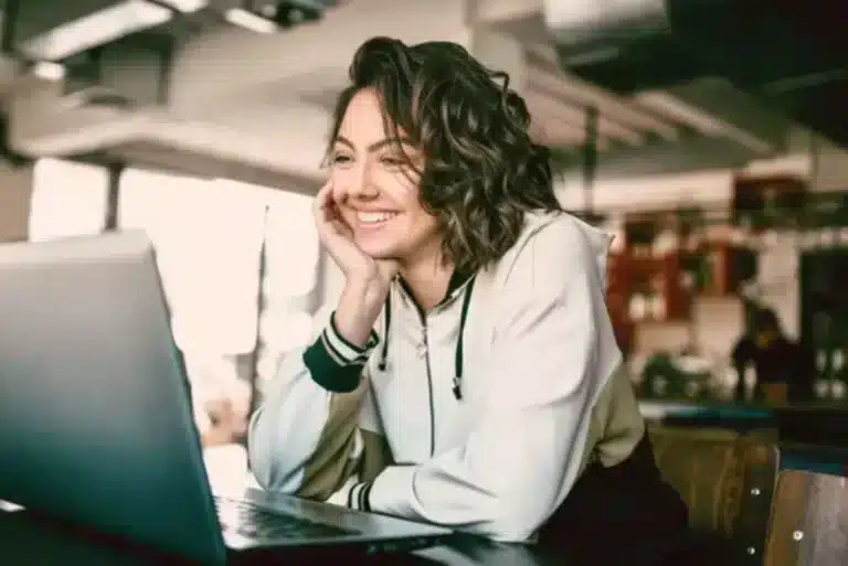 A woman is smiling while using a laptop.