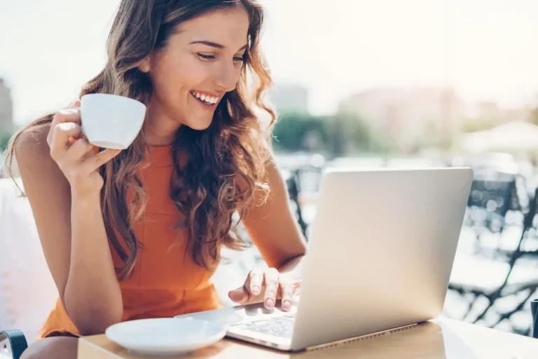 A woman is sitting at a table with a laptop and a cup of coffee.