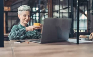 A woman sitting at a desk with a laptop and a cup of coffee.