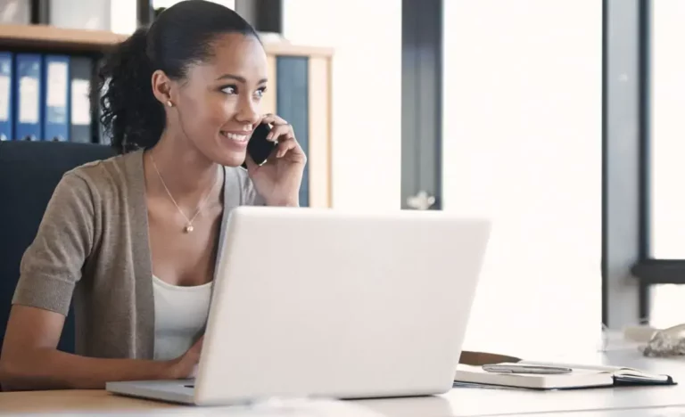 A woman talking on the phone while sitting in front of a laptop.