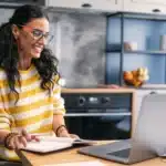 A woman sitting at a table with a laptop and a notebook.